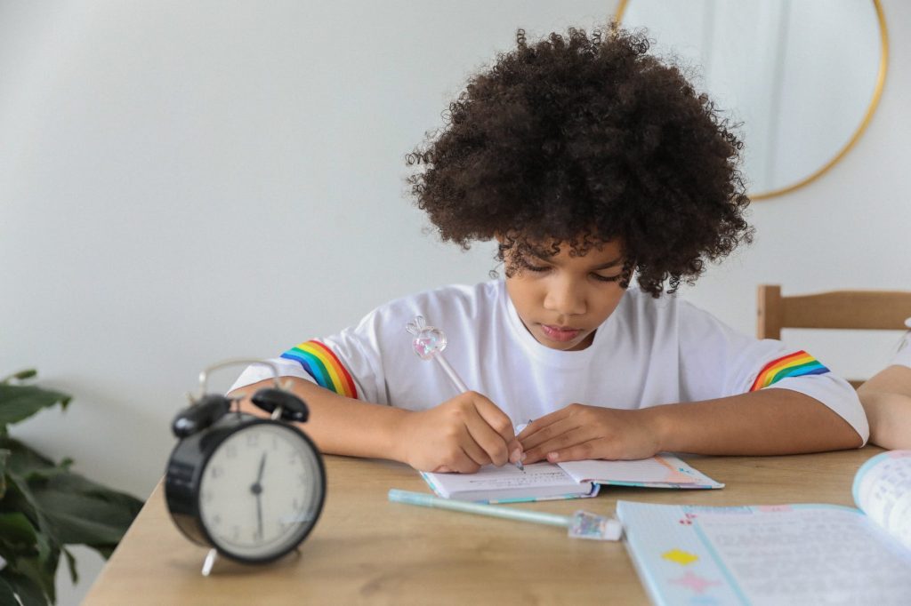 focused black schoolgirl doing homework at table in house