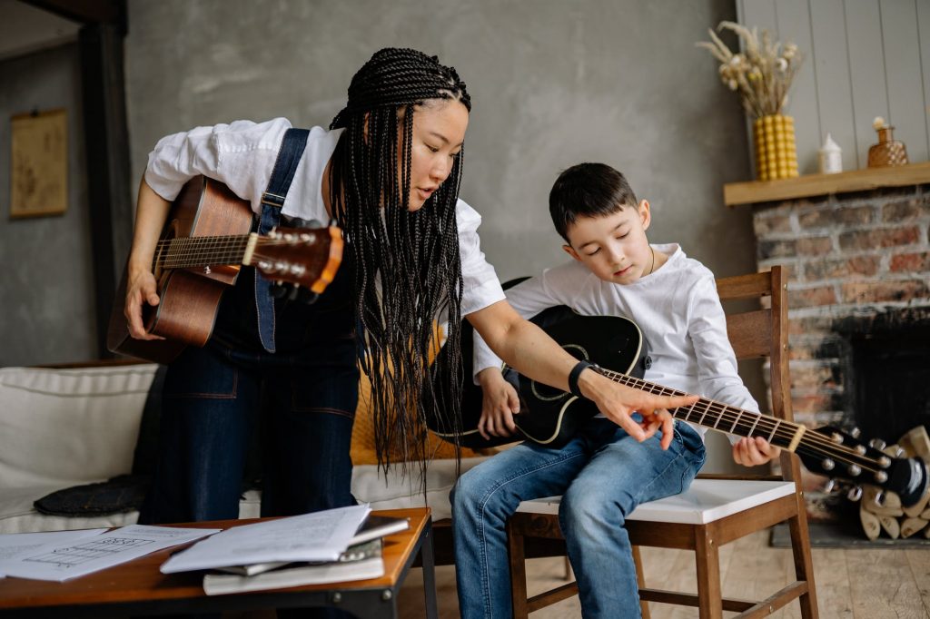 a music instructor with braided hair teaching a boy to play guitar