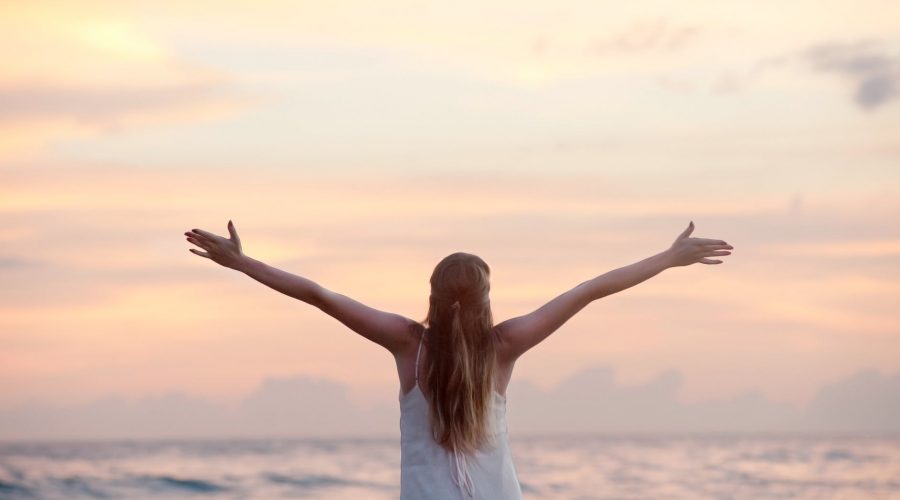 rear view of woman with arms raised at beach during sunset