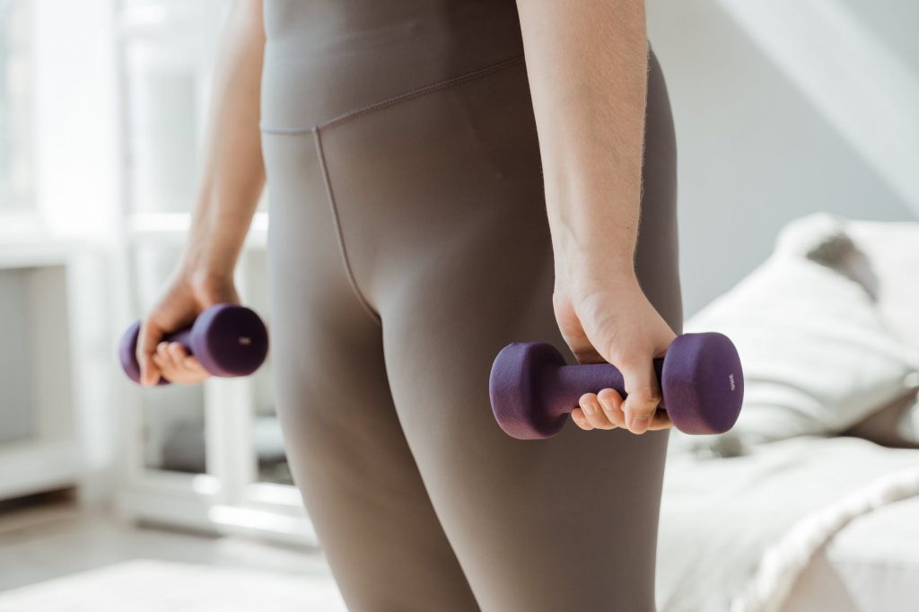 person wearing gray leggings exercising using dumbbells