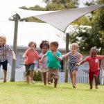 Children playing and laughing outside on a grassy field during school break, with some engaged in running games