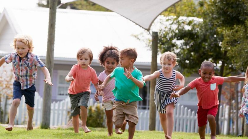 Children playing and laughing outside on a grassy field during school break, with some engaged in running games