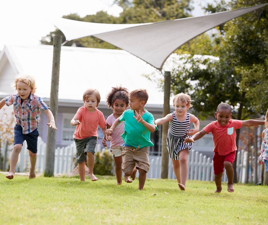 Children playing and laughing outside on a grassy field during school break, with some engaged in running games