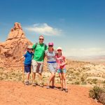 A family of four posing on desert-like ground before a large red rock formation in Zion National Park.