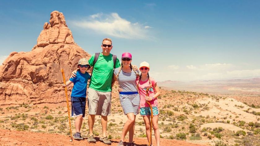 A family of four posing on desert-like ground before a large red rock formation in Zion National Park.