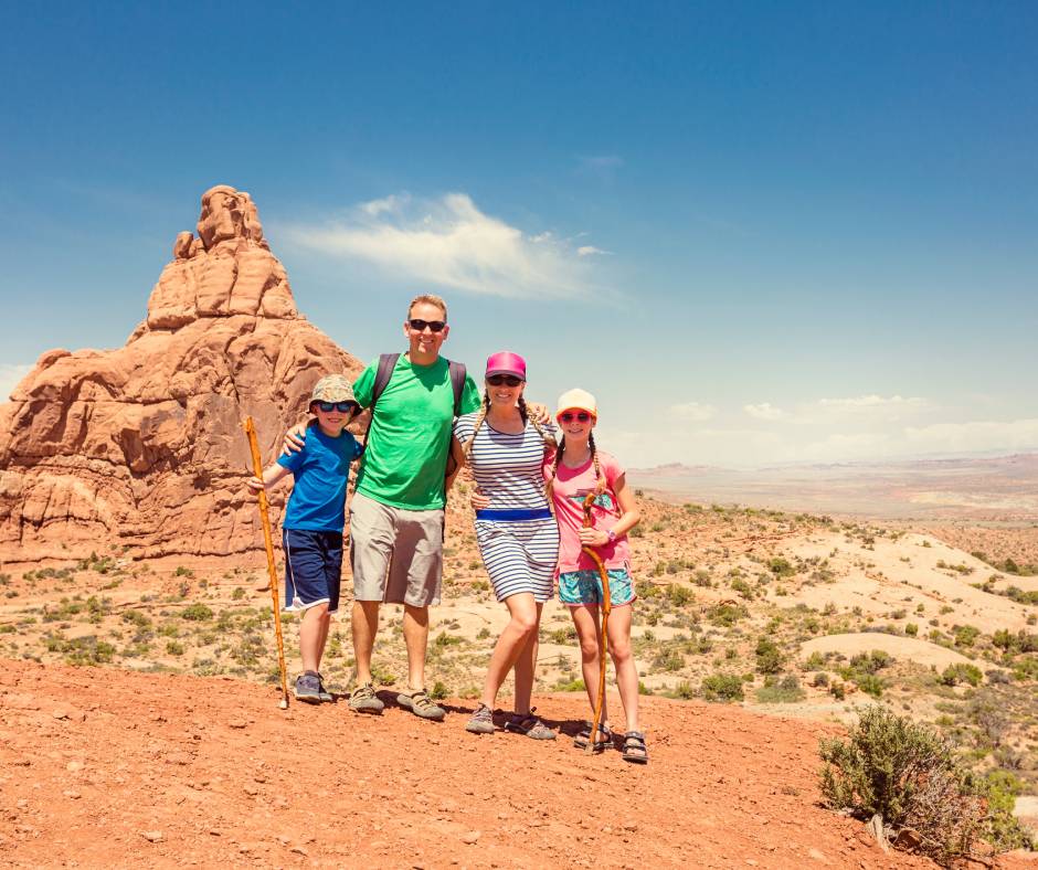 A family of four posing on desert-like ground before a large red rock formation in Zion National Park.