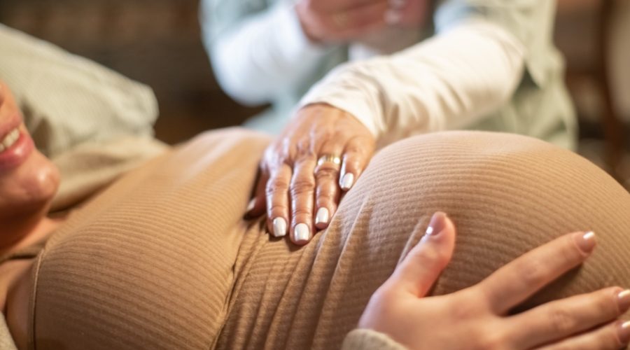 A midwife offering a hand to a pregnant mother before birth. The mother is wearing comfortable clothing.