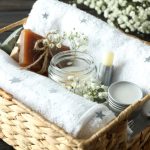 A wicker basket containing a variety of gifts from a candle, homemade chapstick, towels, and a homemade bar of soap.