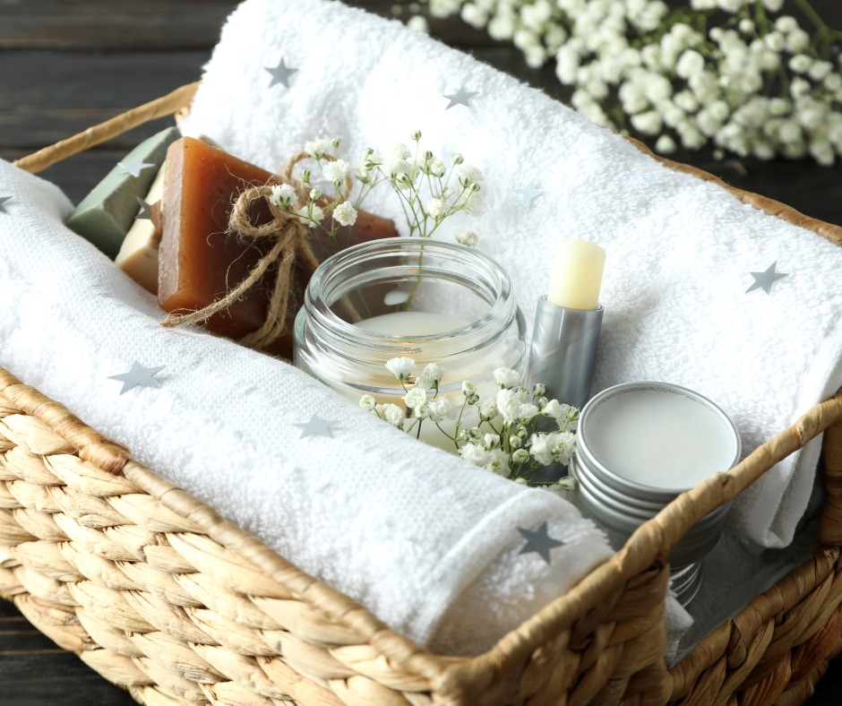 A wicker basket containing a variety of gifts from a candle, homemade chapstick, towels, and a homemade bar of soap.