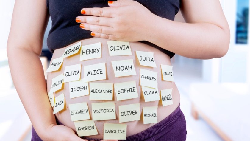 Closeup of a woman holding her pregnant belly that is covered with yellow post-it notes with different name options.