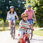 A family consisting of a mom, dad, and little boy riding bikes together down a path. They each wear a helmet.