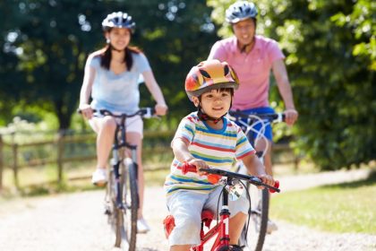 A family consisting of a mom, dad, and little boy riding bikes together down a path. They each wear a helmet.