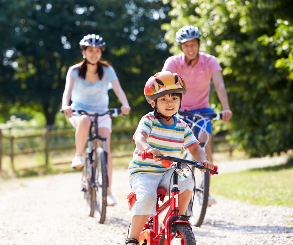 A family consisting of a mom, dad, and little boy riding bikes together down a path. They each wear a helmet.