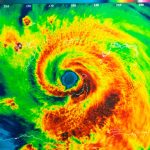 A storm radar depicting the swirling clouds of a hurricane in red, orange, and green. The rest of the radar is blue.