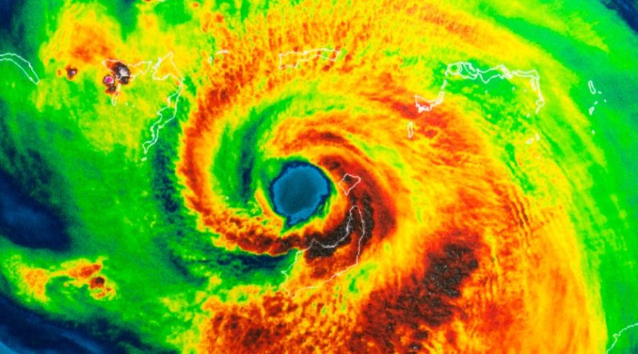 A storm radar depicting the swirling clouds of a hurricane in red, orange, and green. The rest of the radar is blue.