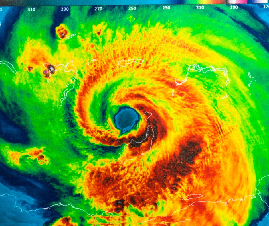 A storm radar depicting the swirling clouds of a hurricane in red, orange, and green. The rest of the radar is blue.