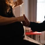 A close-up on a pregnant woman's belly as she holds a person's hand standing next to her in support.