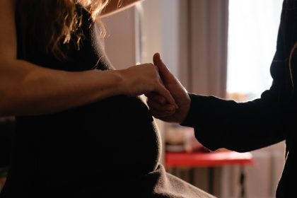 A close-up on a pregnant woman's belly as she holds a person's hand standing next to her in support.