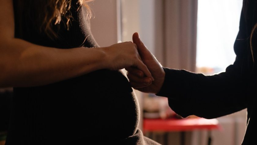 A close-up on a pregnant woman's belly as she holds a person's hand standing next to her in support.