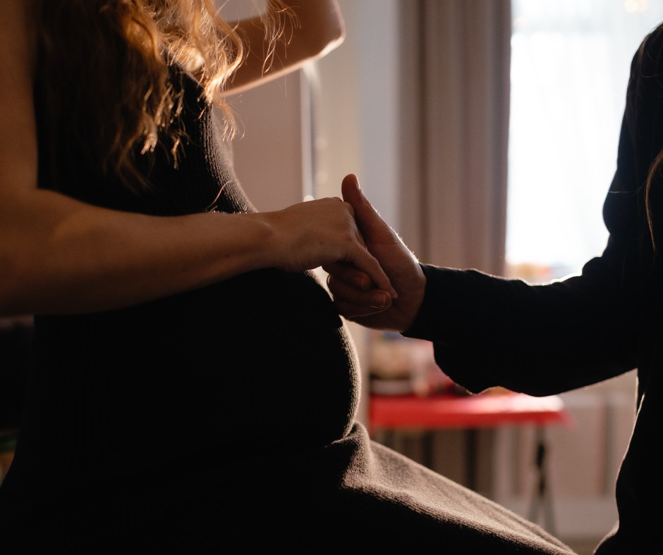 A close-up on a pregnant woman's belly as she holds a person's hand standing next to her in support.