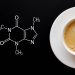 A cup of coffee on a plate that is next to a written formula for anhydrous caffeine. The plate and cup are white.