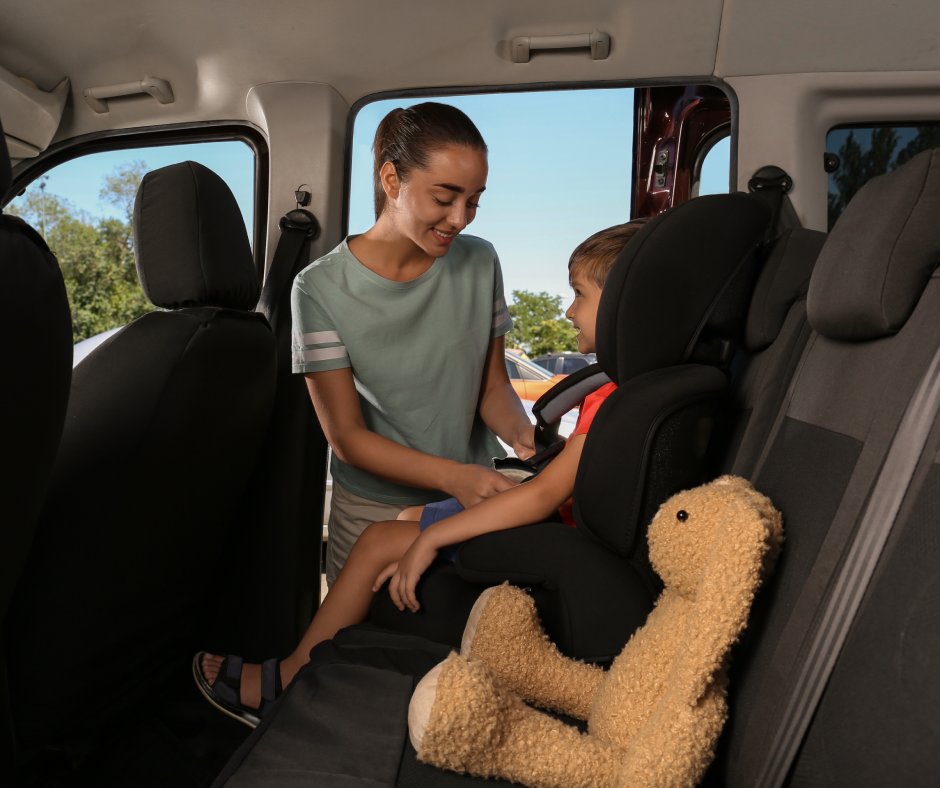 A young mother buckling up her child in the backseat of a car with a brown rabbit stuffed animal next to him.