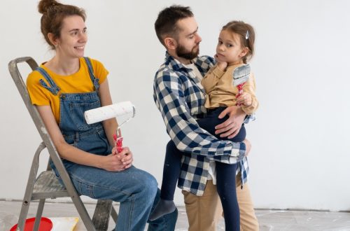 Two happy young parents with their daughter holding a paintbrush. The mother sits on a step ladder and holds a paint roller.