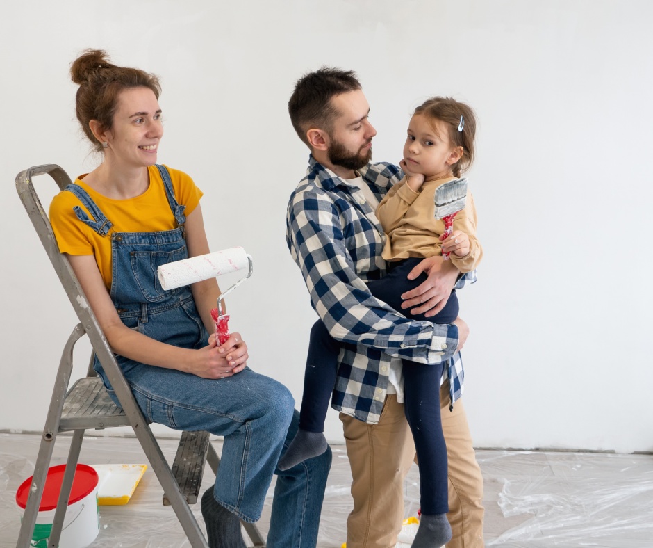 Two happy young parents with their daughter holding a paintbrush. The mother sits on a step ladder and holds a paint roller.