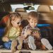 A young boy and girl sitting in the back of a vehicle that’s packed for vacation while looking at a tablet.