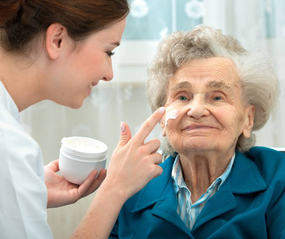 A woman putting facial cream on an elderly woman. The elderly woman is wearing a blue jacket.