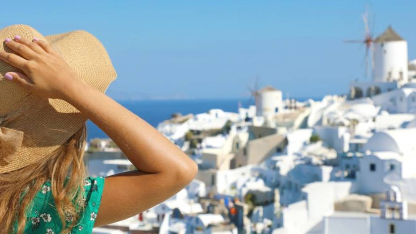 A woman wearing a hat and a green shirt outside looking at some white houses. She has long hair.