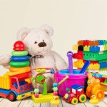 Children's toys, including a stuffed bear, plastic truck, building blocks, and sand buckets, sit on a wooden floor.