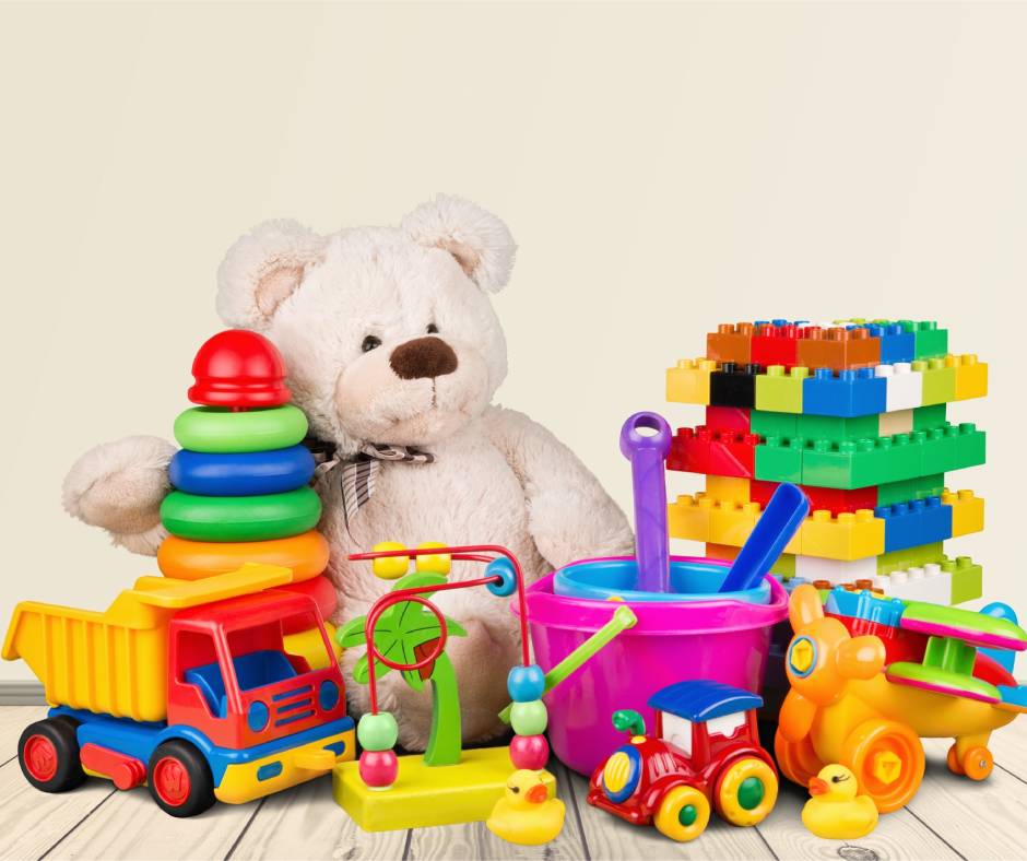 Children's toys, including a stuffed bear, plastic truck, building blocks, and sand buckets, sit on a wooden floor.