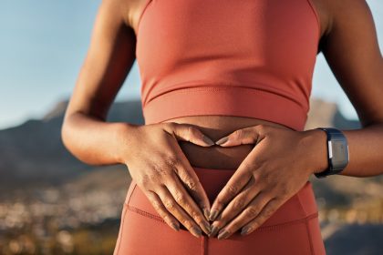 A woman in fitness apparel holding her hands over her stomach while wearing a watch and mountain ridges behind her.