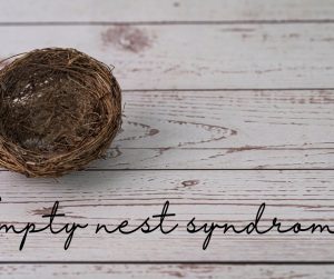A small empty bird nest sitting on a wooden surface. Underneath it are the words "empty nest syndrome."
