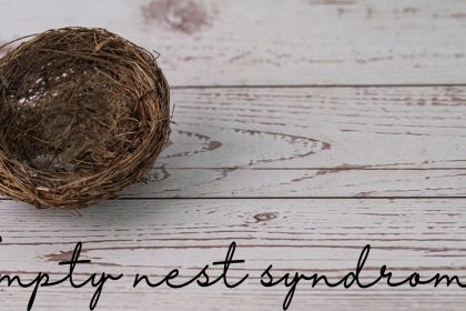 A small empty bird nest sitting on a wooden surface. Underneath it are the words "empty nest syndrome."