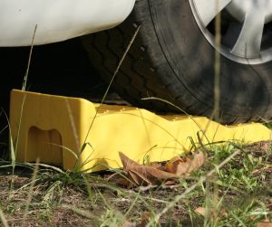A close-up view shows the tire of a vehicle being stopped by a yellow block on a grassy surface.