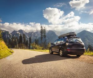 A black compact SUV parks on the side of the road, with a stretch of mountainous terrain visible in the distance.