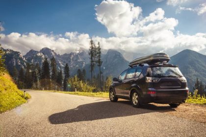 A black compact SUV parks on the side of the road, with a stretch of mountainous terrain visible in the distance.