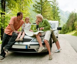 A family with two children gathering on the front of a parked vehicle to look over a roadmap together.