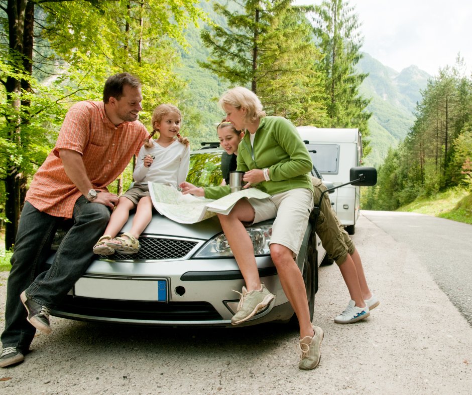 A family with two children gathering on the front of a parked vehicle to look over a roadmap together.