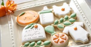 A plate of frosted sugar cookies for a gender-neutral baby shower. One cookie says, "A little cutie is on the way."