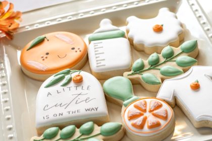 A plate of frosted sugar cookies for a gender-neutral baby shower. One cookie says, "A little cutie is on the way."