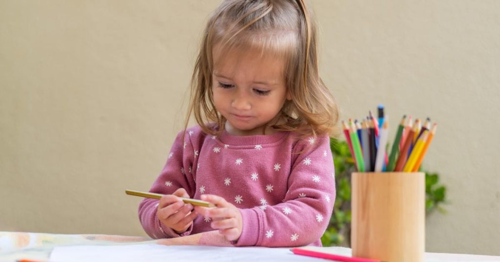 A young girl is participating in a drawing activity with colored pencils at a table in an early childhood education program.