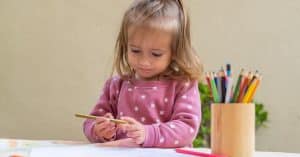 A young girl is participating in a drawing activity with colored pencils at a table in an early childhood education program.