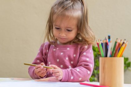 A young girl is participating in a drawing activity with colored pencils at a table in an early childhood education program.