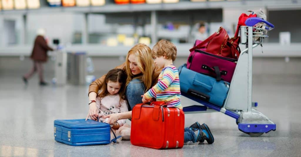 A mother helps one of her two children with a suitcase in the middle of an airport. A luggage trolley sits behind them.