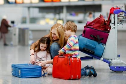A mother helps one of her two children with a suitcase in the middle of an airport. A luggage trolley sits behind them.