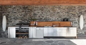 Several kitchen appliances are against a wall. There are long, cylindrical lights hanging down on either side of the kitchenware.