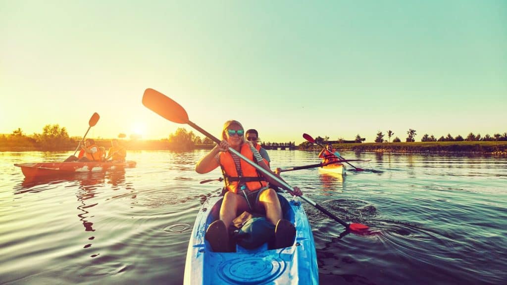 A blonde woman and a Caucasian man are in a blue kayak. A child sits on the woman's lap, holding a paddle.